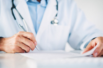 Close up of doctor reading and signing files and paperwork of patient