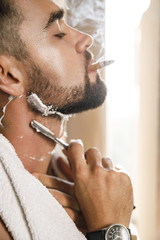 Man smoking a cigarette and shaving his beard with a straight razor