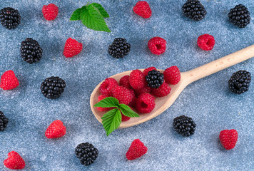 raspberries and blackberries in a wooden spoon on a blue background