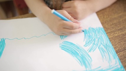 Girl draws with a blue felt-tip pen makes an artistic drawing of the ocean or sea on a white sheet. Hand of a girl with felt-tip pen close-up. Child's drawing