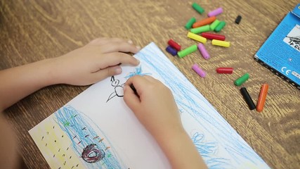 The child draws with black chalk for drawing makes an artistic drawing of a black bird on a white sheet. Child's hand with a chalk for drawing close-up. Child's drawing