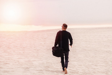 man walking in a desert with black bag - Powered by Adobe