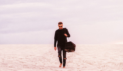 man walking in a desert with black bag