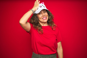 Middle age senior woman wearing cute kitty cap over red isolated background stressed with hand on head, shocked with shame and surprise face, angry and frustrated. Fear and upset for mistake.