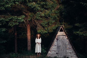 Woman pretty wear amazing white dress and hat on forest and wooden wigwam background . Perfect plase for ceremony. © gartmanart