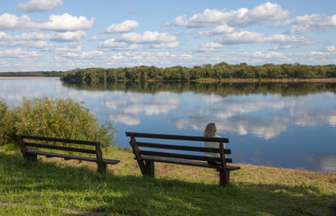 Beautiful landscape with river and clouds  and the girl on the bench
