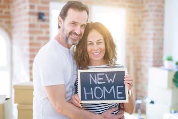 Middle age senior couple moving to a new house, smiling happy in love with apartmant holding a blackboard with new home text