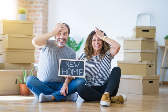 Middle age senior couple sitting on the floor holding blackboard moving to a new home stressed with hand on head, shocked with shame and surprise face, angry and frustrated