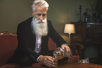 Handsome bearded senior man pouring whiskey into the glass