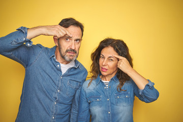 Beautiful middle age couple together standing over isolated yellow background pointing unhappy to pimple on forehead, ugly infection of blackhead. Acne and skin problem