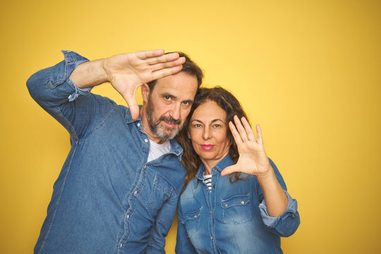 Beautiful middle age couple together standing over isolated yellow background doing frame using hands palms and fingers, camera perspective