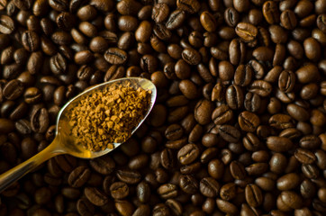 Instant granulated coffee in the spoon at the background of aromatic coffee beans, close-up image with a copyspace for a text