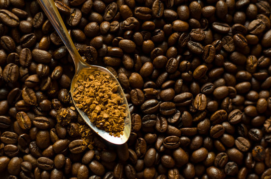 Instant granulated coffee in the spoon at the background of aromatic coffee beans, close-up image with a copyspace for a text