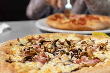 Tasty italian pizza served on a table in restaurant and blurred man eating pizza on background
