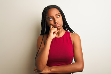 African american woman wearing red casual t-shirt standing over isolated white background with hand on chin thinking about question, pensive expression. Smiling with thoughtful face. Doubt concept.