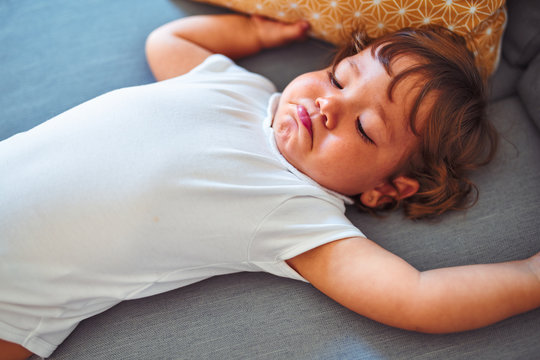 Beautiful toddler child girl wearing white bodysuit lying down on the sofa