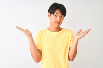 Chinese man wearing yellow casual t-shirt standing over isolated white background clueless and...