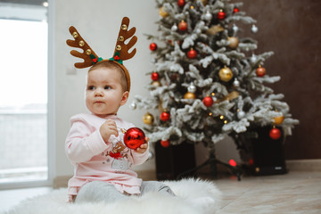 Happy child with deer horns near a Christmas tree.