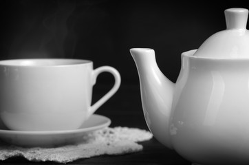 cup of hot tea and teapot. White set on a black table. Closeup