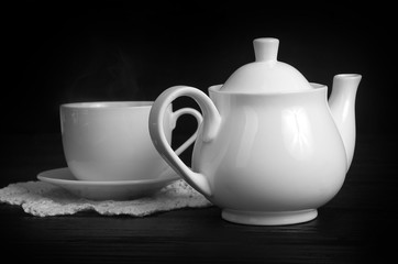 cup of hot tea and white teapot on a black table