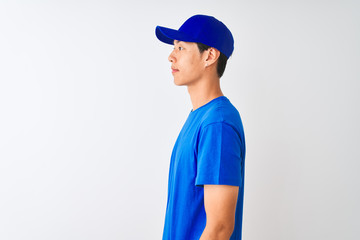 Chinese deliveryman wearing blue t-shirt and cap standing over isolated white background looking to side, relax profile pose with natural face with confident smile.