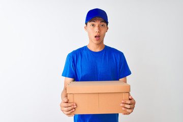 Chinese deliveryman wearing cap holding box standing over isolated white background scared in shock with a surprise face, afraid and excited with fear expression