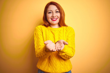 Beautiful redhead woman wearing winter sweater standing over isolated yellow background Smiling with hands palms together receiving or giving gesture. Hold and protection