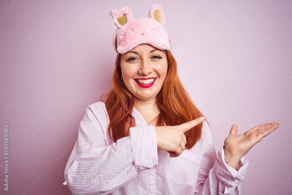 Sticker Young beautiful redhead woman wearing pajama over pink isolated background amazed and smiling to the camera while presenting with hand and pointing with finger.