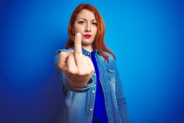 Young beautiful redhead woman wearing denim shirt standing over blue isolated background Showing middle finger, impolite and rude fuck off expression