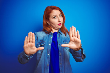 Young beautiful redhead woman wearing denim shirt standing over blue isolated background Moving...
