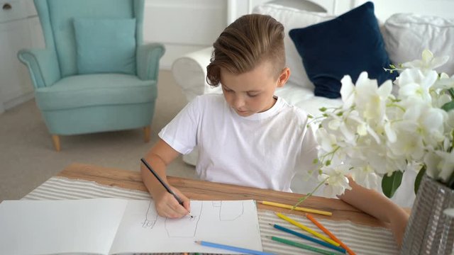 Seven years boy drawing picture with pencils of different colors in living room