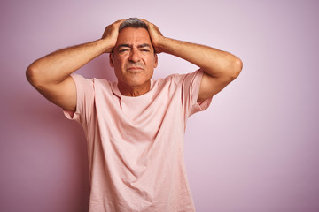 Handsome middle age man wearing t-shirt standing over isolated pink background suffering from headache desperate and stressed because pain and migraine. Hands on head.
