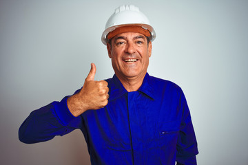 Handsome middle age worker man wearing uniform and helmet over isolated white background doing happy thumbs up gesture with hand. Approving expression looking at the camera showing success.