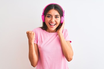 Young beautiful woman listening to music using headphones over isolated white background screaming proud and celebrating victory and success very excited, cheering emotion