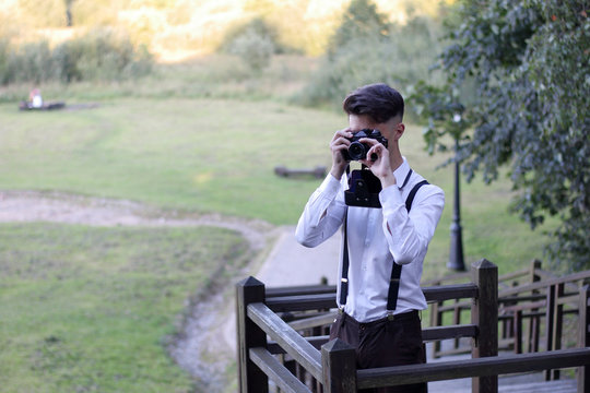 Stylishly dressed young man sits taking pictures in the park. In his hands holds a SLR film camera.