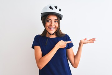 Young beautiful cyclist woman wearing security bike helmet over isolated white background amazed and smiling to the camera while presenting with hand and pointing with finger.