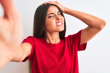 Fototapeta na wymiar Beautiful woman wearing red t-shirt make selfie by camera over isolated white background stressed with hand on head, shocked with shame and surprise face, angry and frustrated.