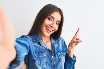 Beautiful woman wearing denim shirt make selfie by camera over isolated white background with a big...