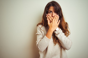 Young beautiful woman wearing winter sweater standing over white isolated background shocked covering mouth with hands for mistake. Secret concept.