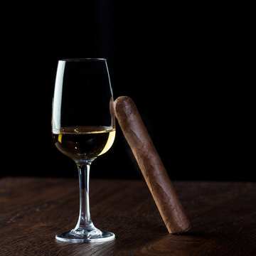 Picture of a Cuban cigar relied on on a glass of white wine,on the wooden table,luxury and well being life concept