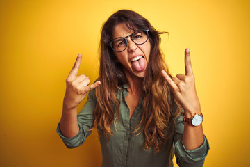 Young beautiful woman wearing green shirt and glasses over yelllow isolated background shouting...