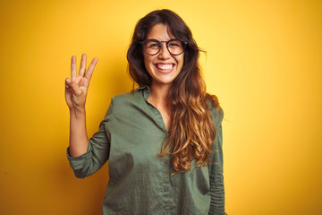 Young beautiful woman wearing green shirt and glasses over yelllow isolated background showing and...