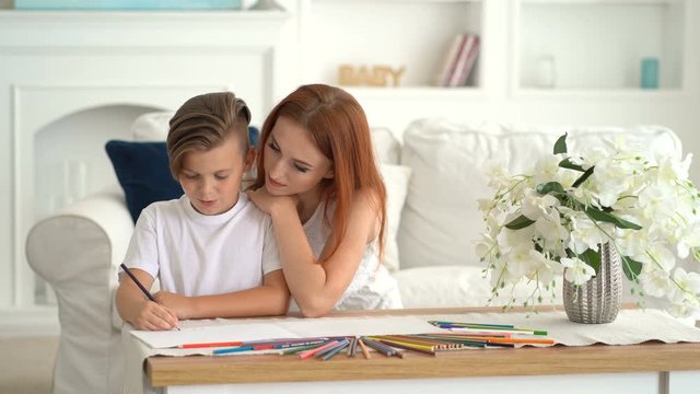 mom watches her son draw with сolored pencils