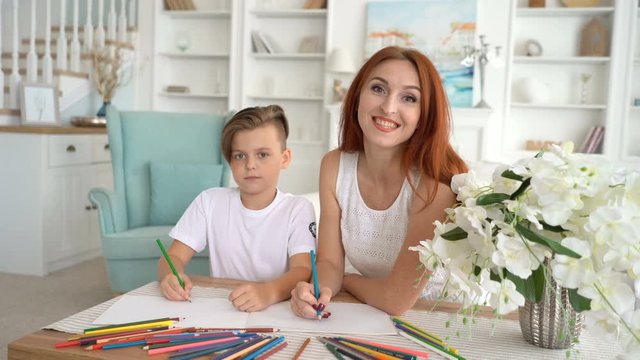 Red-haired mother and her son with a fashionable hairstyle draw at home