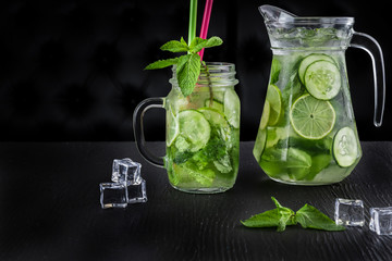 Retro glass jar and jug of lemonade with cucumber and mint on wooden table. Cubes of ice