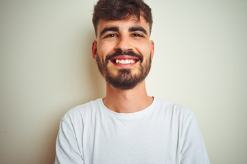 Obraz premium Young man with tattoo wearing t-shirt standing over isolated white background happy face smiling with crossed arms looking at the camera. Positive person.