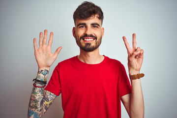 Young man with tattoo wearing red t-shirt standing over isolated white background showing and pointing up with fingers number seven while smiling confident and happy.