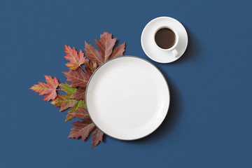 Autumn coffee cup and empty plate with coloured maple feaf on dark blue background, Flat Lay with Copy Space