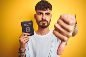 Young man with tattoo wearing Italy Italian passport over isolated yellow background with angry...