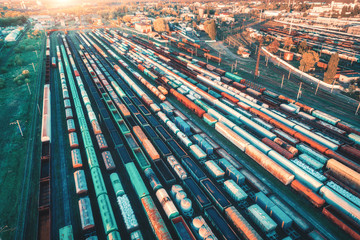 Aerial view of freight trains. Colorful cargo wagons on railway station. Wagons with goods on railroad. Heavy industry. Industrial landscape with train, railway platfform at sunset. Top view. Depot